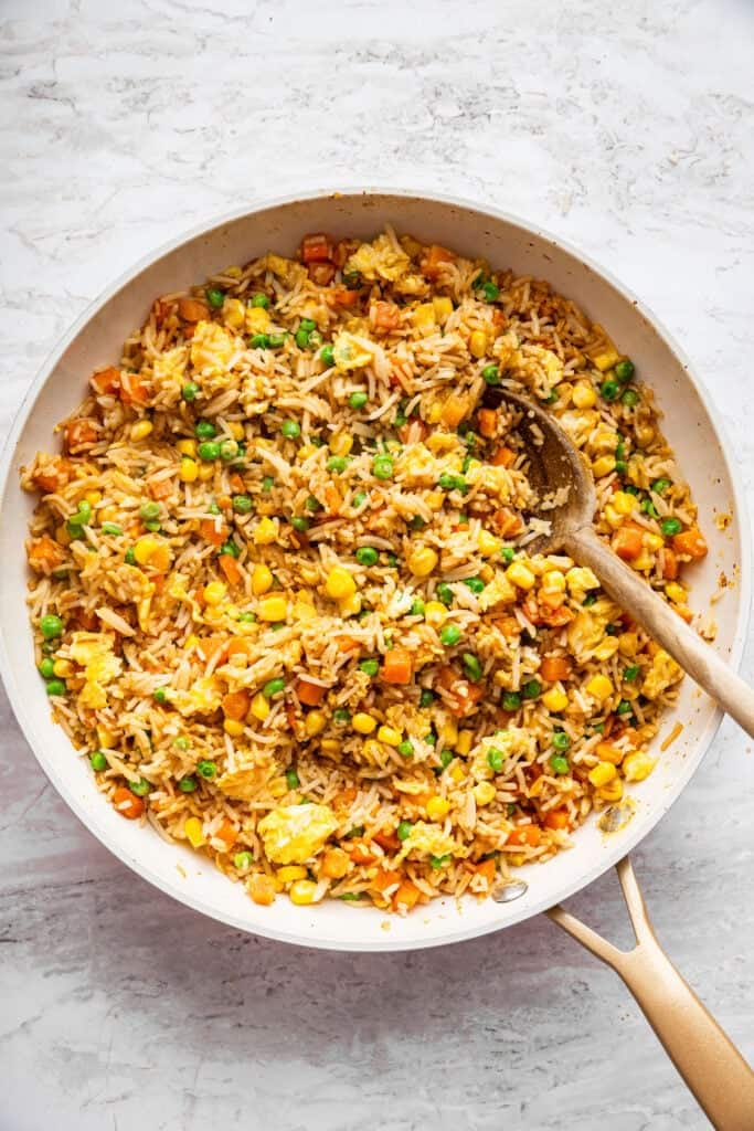 This 10-minute vegetable fried rice is the ultimate quick meal or side dish! Easy, flavorful, and perfect for busy weeknights. Wooden spoon in skillet of vegetable fried rice.