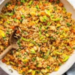 Skillet of vegetable fried rice with wooden spoon.