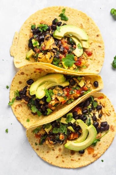 Overhead view of three breakfast tacos topped with avocado slices and cilantro.
