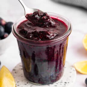 Spoon of blueberry compote held over jar.