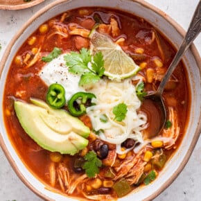Overhead view of chicken taco soup in a bowl, garnished with avocado, cilantro, cheese, sour cream, and lime