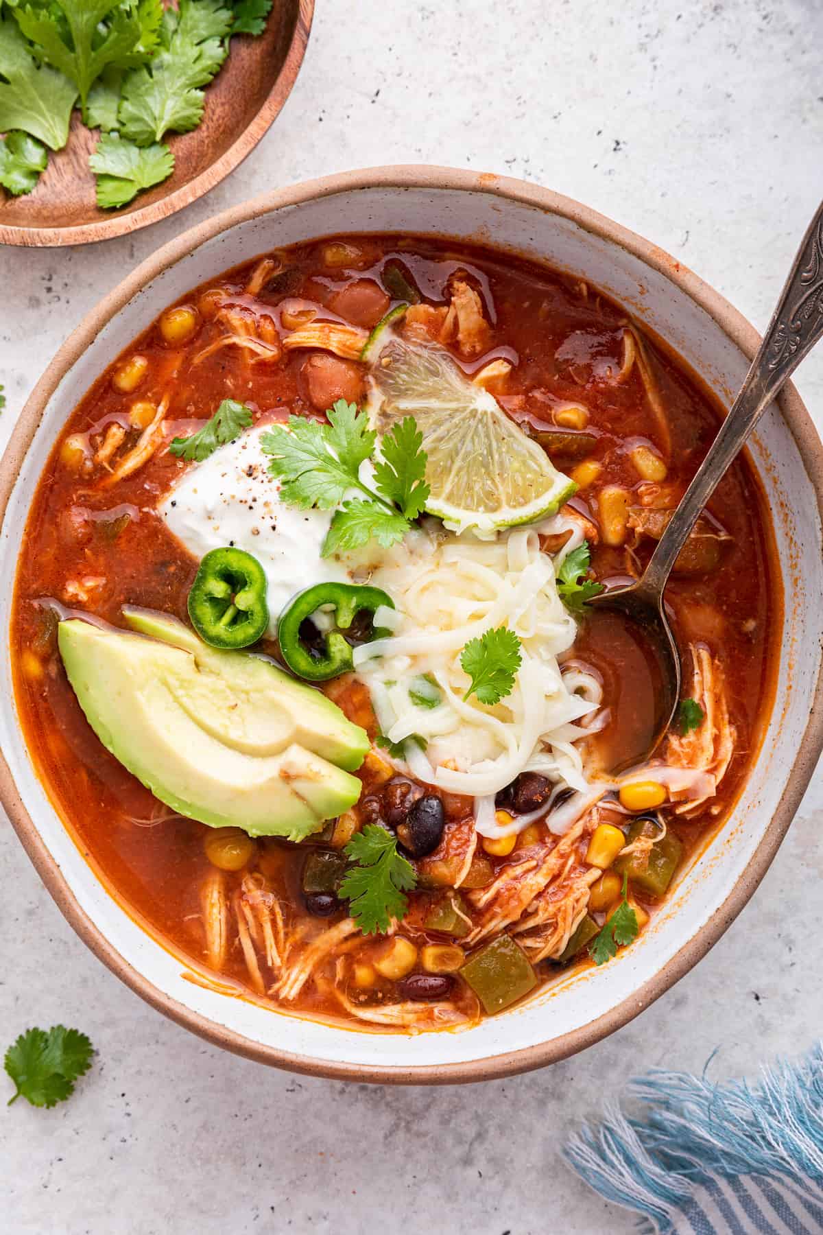 Overhead view of chicken taco soup in a bowl, garnished with avocado, cilantro, cheese, sour cream, and lime