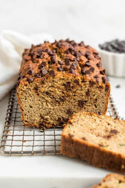 A chocolate chip zucchini loaf on a cooling rack with a couple of slices cut from it.