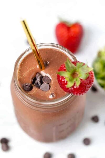 Overhead view of a chocolate strawberry smoothie in a glass jar garnished with chocolate chips and a fresh berry.