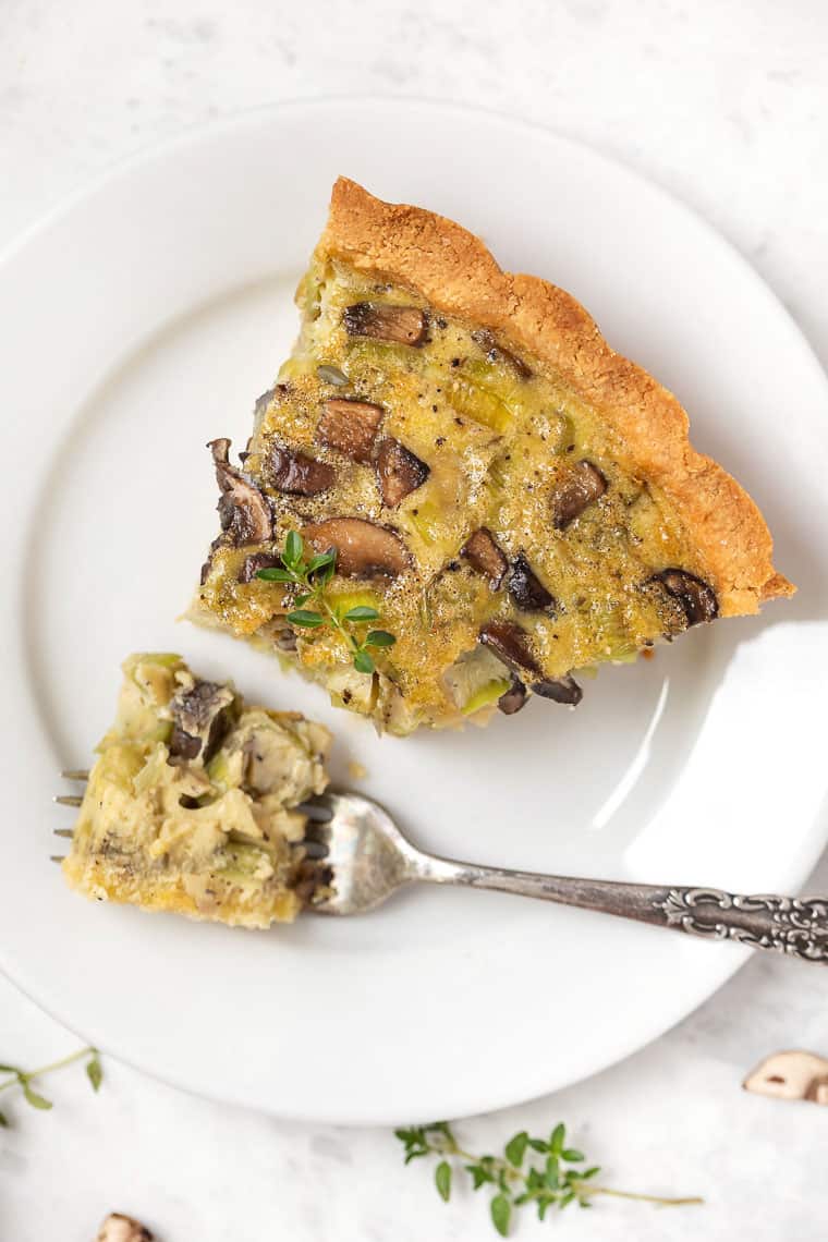 Slice of mushroom quiche on plate with tip of quiche on fork