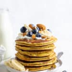 A stack of protein pancakes on a plate topped with fresh fruit and nuts.