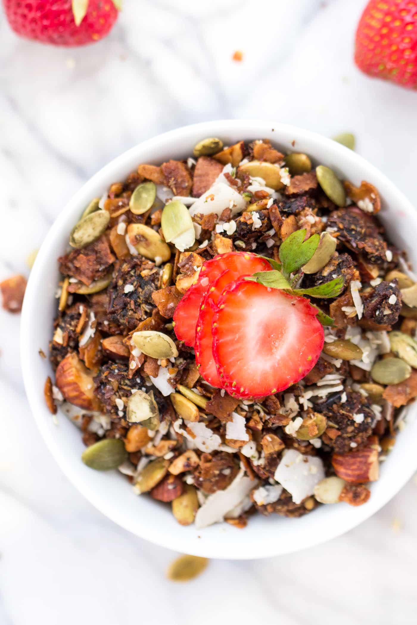 This grain-free coconut granola is the ultimate breakfast treat! It's crunchy, sweet and made with all-natural ingredients. Paleo + vegan! Coconut granola in bowl topped with sliced strawberry