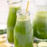 Two glasses of green juice with a pitcher in the background.