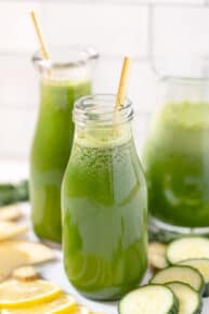 Two glasses of green juice with a pitcher in the background.