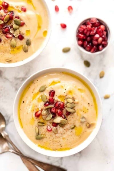 Overhead view of two bowls of creamy cauliflower soup topped with pomegranate seeds and pumpkin seeds.