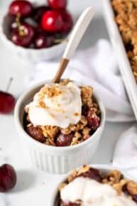 A serving of cherry crumble in a bowl topped with coconut yogurt.