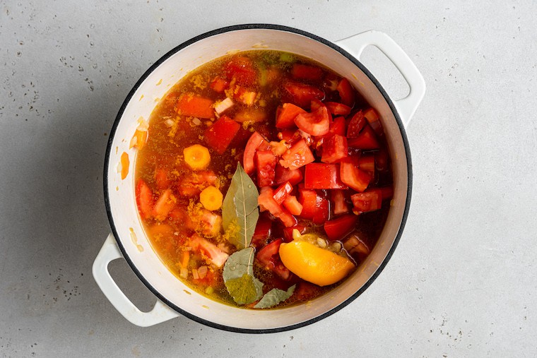 Overhead view of vegetable stew in pot after adding tomatoes, lemon, and bay leaves