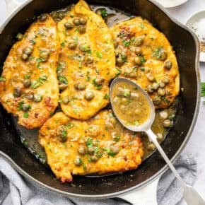 Skillet of lemon caper chicken with spoonful of sauce