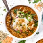 Overhead view of a bowl of Moroccan lentil soup topped with garnishes, with a spoon.