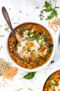 Overhead view of a bowl of Moroccan lentil soup topped with garnishes, with a spoon.