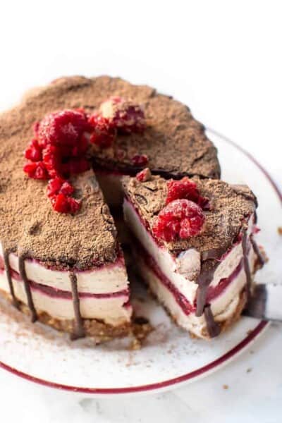 Overhead view of a slice of no bake raspberry cheesecake garnished with chocolate and fresh raspberries being lifted from the rest of the cheesecake with a cake server.