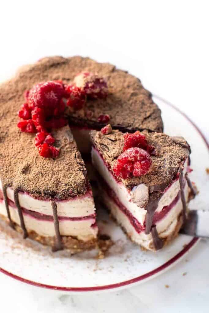 Overhead view of a slice of no bake raspberry cheesecake garnished with chocolate and fresh raspberries being lifted from the rest of the cheesecake with a cake server.