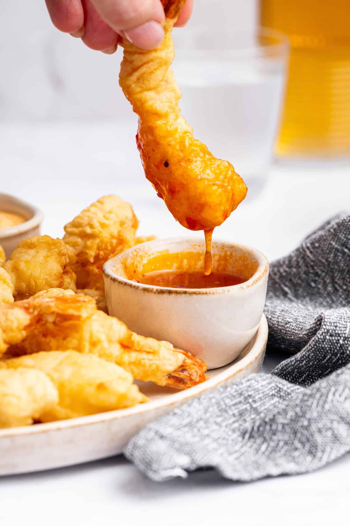 Dredge them in cornstarch. Generously sprinkle cornstarch on your shrimp until they’re completely covered. Shake off any excess. Dipping shrimp tempura into bowl of sauce