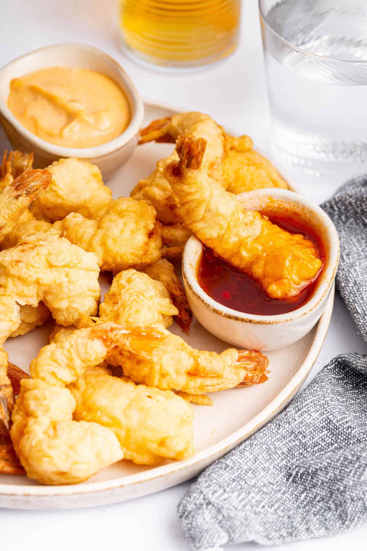 Dredge them in cornstarch. Generously sprinkle cornstarch on your shrimp until they’re completely covered. Shake off any excess. Crispy shrimp tempura on plate with bowls of dipping sauce