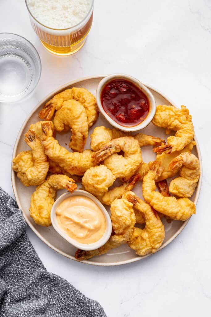 Dredge them in cornstarch. Generously sprinkle cornstarch on your shrimp until they’re completely covered. Shake off any excess. Plate of shrimp tempura with two small bowls of sauce