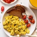 Overhead view of a tofu scramble with roasted tomatoes and two slices of wheat toast on a plate.