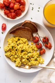Overhead view of a tofu scramble with roasted tomatoes and two slices of wheat toast on a plate.