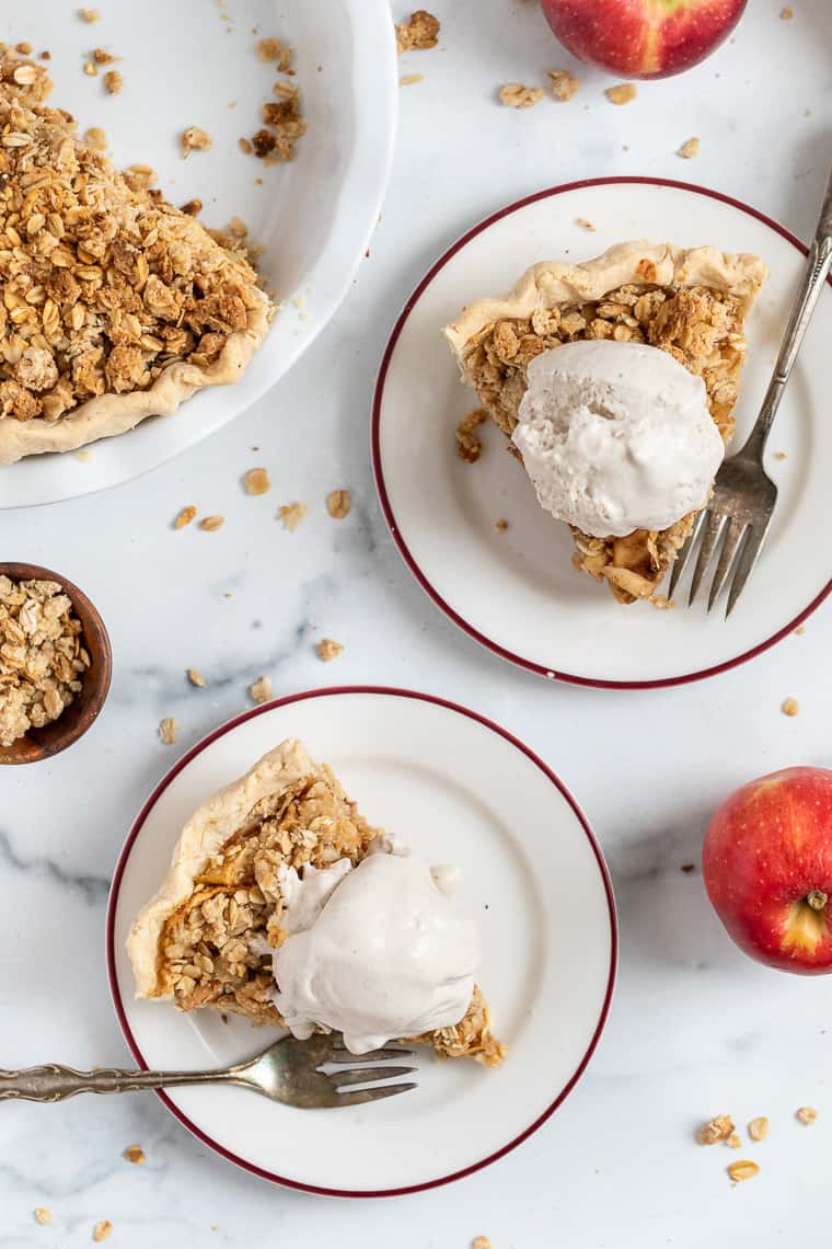 Overhead view of two slices of apple crumb pie topped with ice cream on plates.