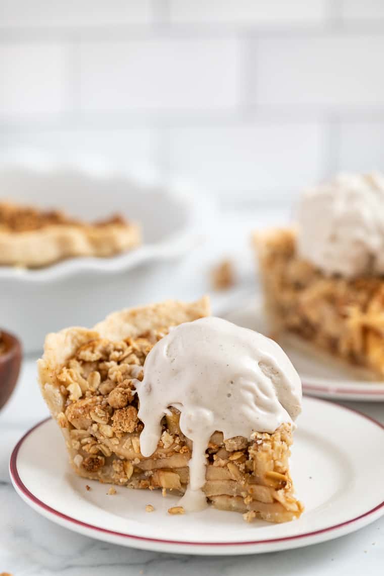A slice of gluten-free and vegan apple crumb pie topped with ice cream on a plate.