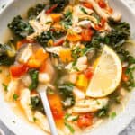 Bowl of chicken vegetable soup with spoon and lemon slice.