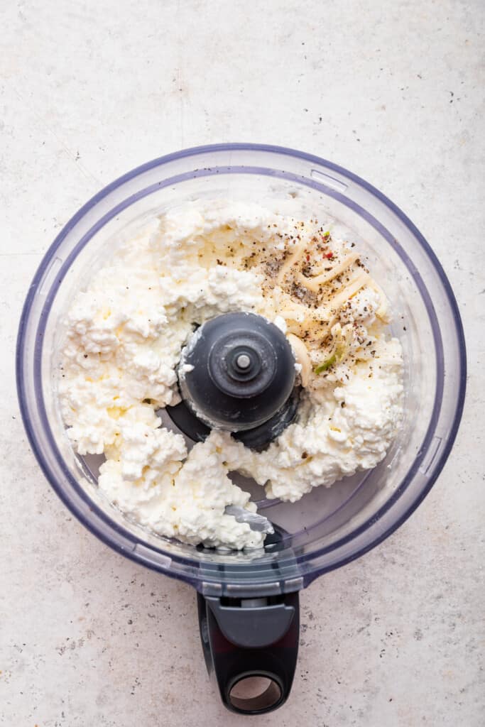 Love the protein but hate the curds? Whipped cottage cheese gives you the nutrition without the texture. Two easy versions: sweet & savory! Overhead view of ingredients for whipped cottage cheese in food processor