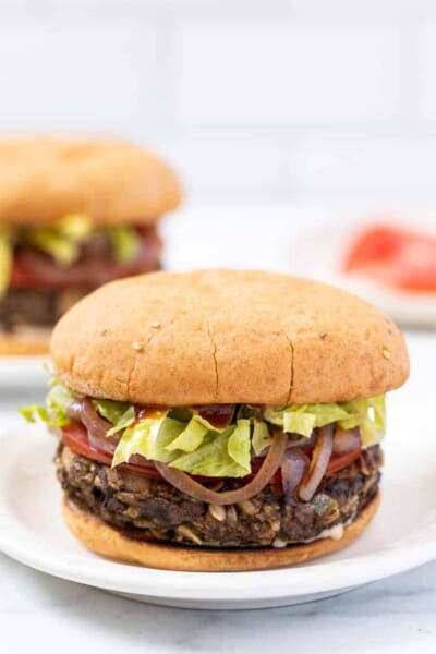 A mushroom veggie burger on a plate with a second burger in the background.