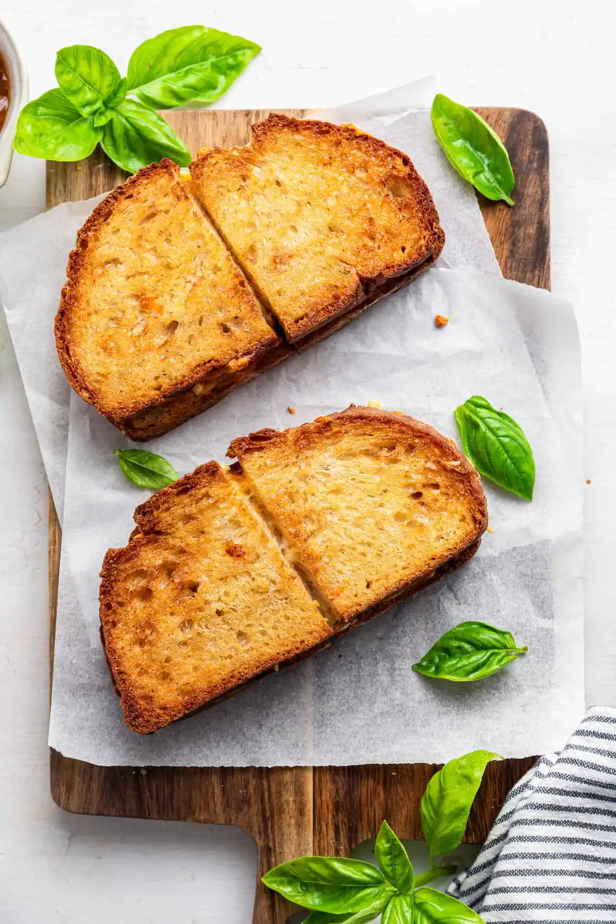 This air fryer grilled cheese recipe makes the BEST sandwich in minutes! Crispy outside, melty inside, and you can make it vegan! Two vegan air fryer grilled cheese sandwiches cut in half on a parchment-lined wooden cutting board.