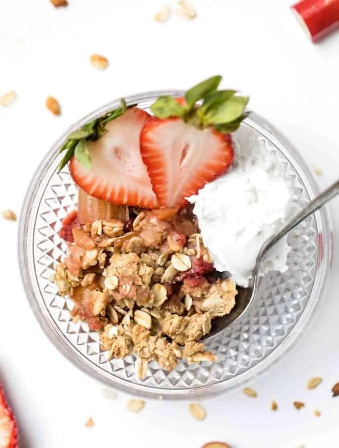 Strawberry rhubarb crisp in bowl with scoop of coconut cream