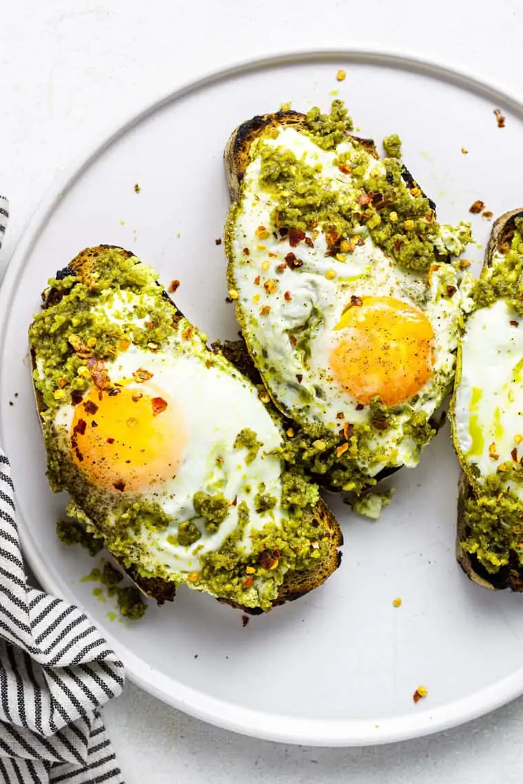 Pesto eggs are a savory high-protein breakfast with avocado toast vibes but MUCH more flavor. Best of all, it comes together in minutes! close up on toast topped with pesto and fried eggs