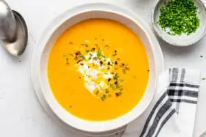 Bowl of sweet potato ginger soup with coconut milk, chives, and red pepper flakes for garnish.