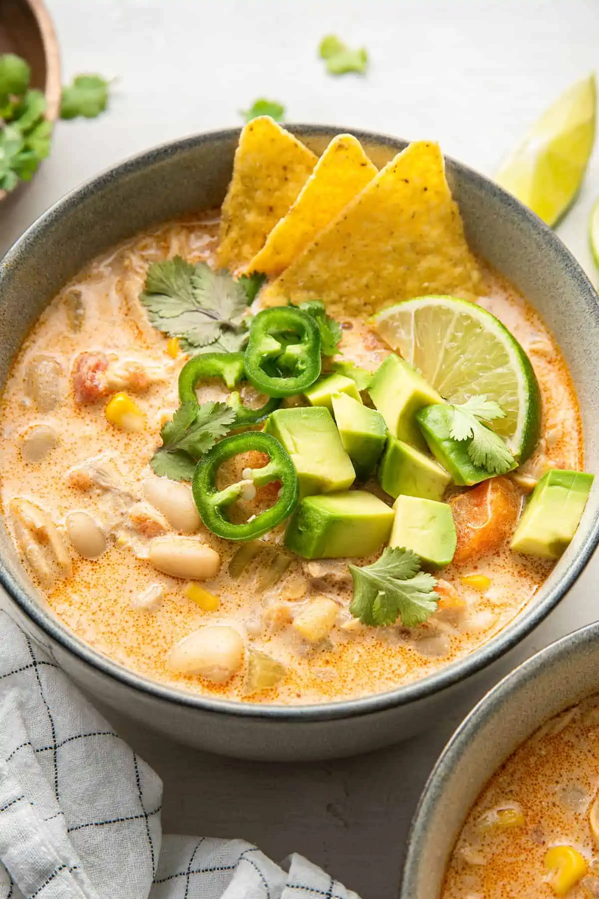 This Instant Pot white chicken chili recipe is rich, hearty, and comforting, with the perfect amount of spice from fresh jalapeños. Close up of a bowl of white chicken chili garnished with tortilla chips, a lime wedge, cilantro, and chunks of avocado and chilis