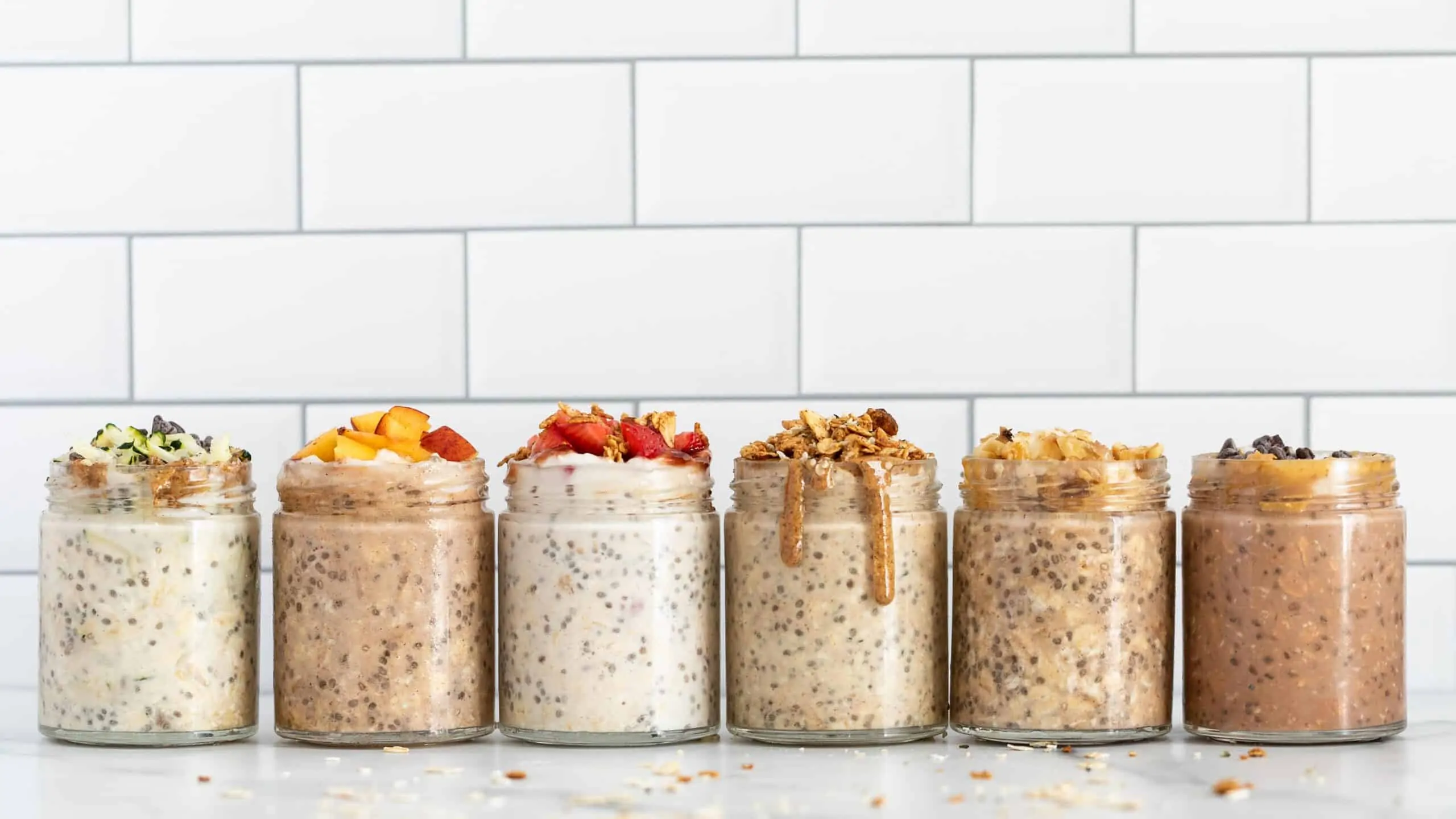 See how to make overnight oats 6 different ways! These easy overnight oats recipes are healthy, full of flavor & perfect for busy mornings. 6 mason jars on a marble counter filled with overnight oats and various toppings